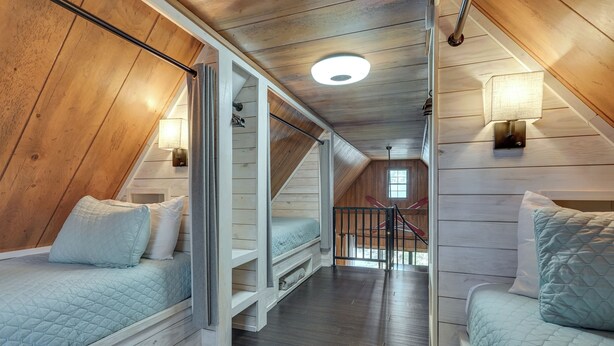 Quarto em estilo loft com duas camas, paredes de madeira, escada e claraboia.