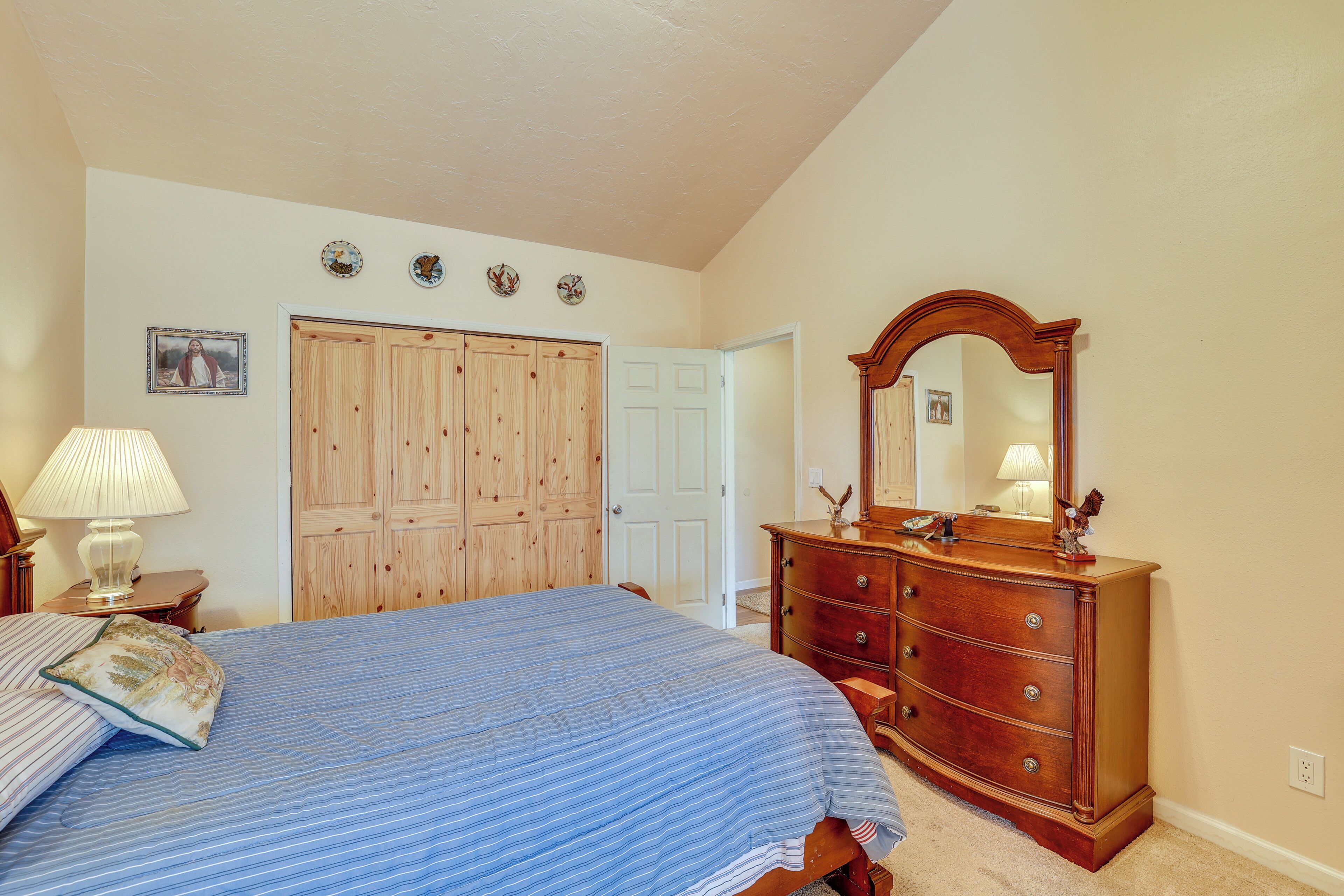 A bedroom with a bed, dresser, mirror, and wooden wardrobe.