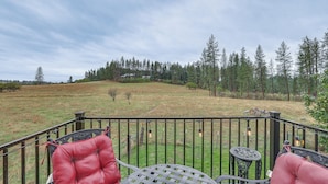 A deck with two chairs and a table, overlooking a grassy field and a forested hill. - Cozy Clearwater Apartment - Hike, Fish & Explore! (Stites)