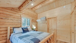 A wooden cabin bedroom with a bed, a window, and a door. - Woodsy Cabin Near Kenai River: Great for Anglers! (Soldotna)