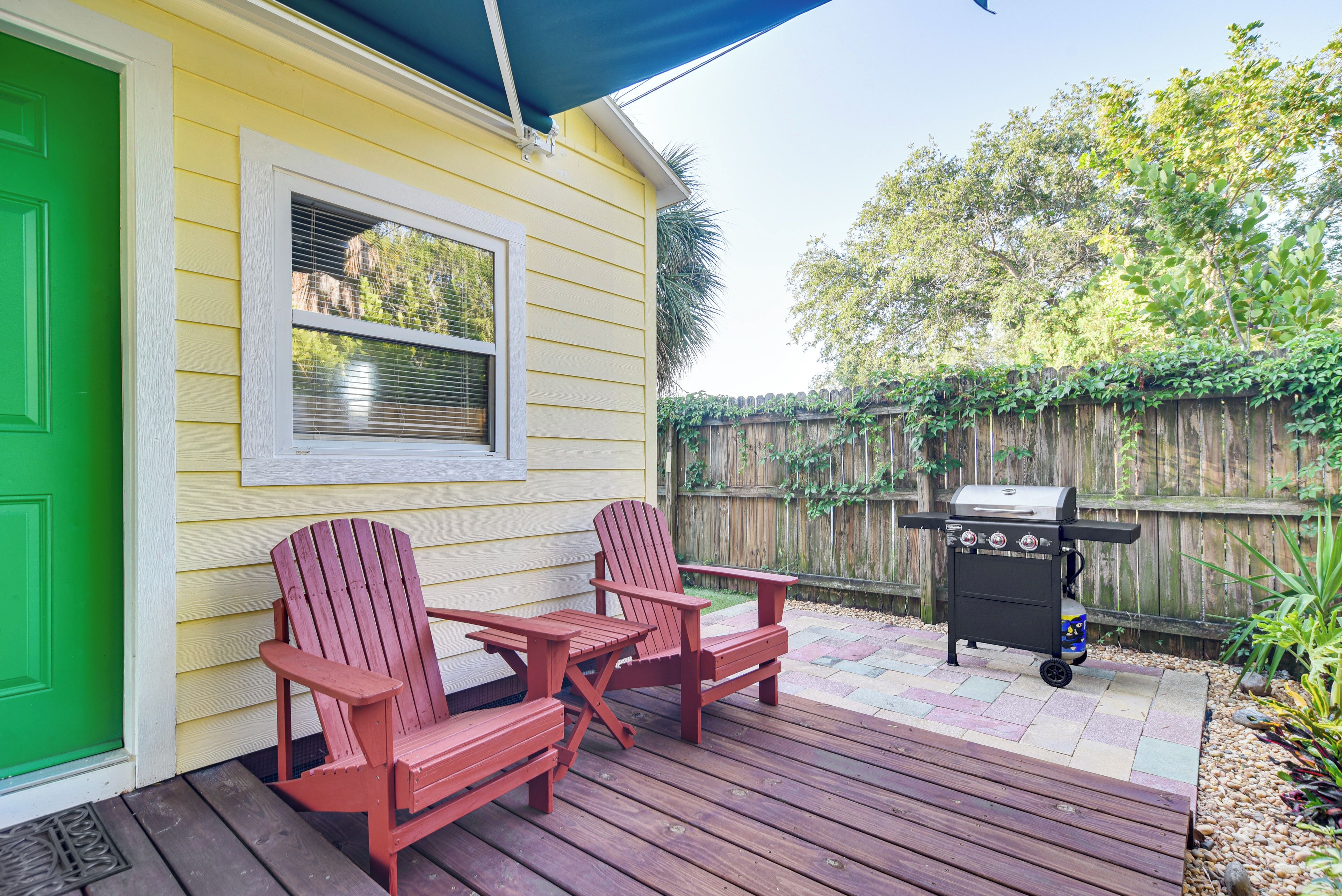 A deck with two Adirondack chairs, a grill, and a green door.