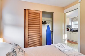 Ein Hotelzimmer mit Bett, einer Holztür, einem blauen Surfbrett und Blick auf die Küche.