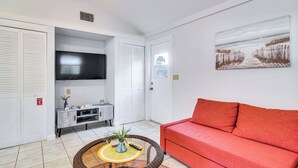 A living room with a red sofa, a flat-screen TV mounted on the wall, a small console table with decorative items, and a painting on the wall. - Cozy St Pete Home ~ 2 Mi to Madeira Beach! (St. Petersburg)
