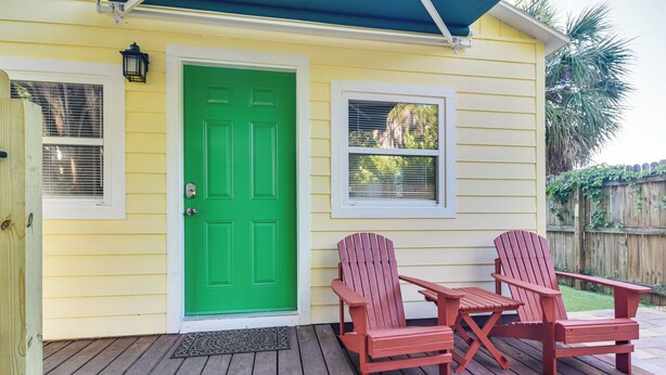 A yellow house with a green door, two red Adirondack chairs, and a small table on a wooden deck. - Cozy St Pete Home ~ 2 Mi to Madeira Beach! (St. Petersburg)