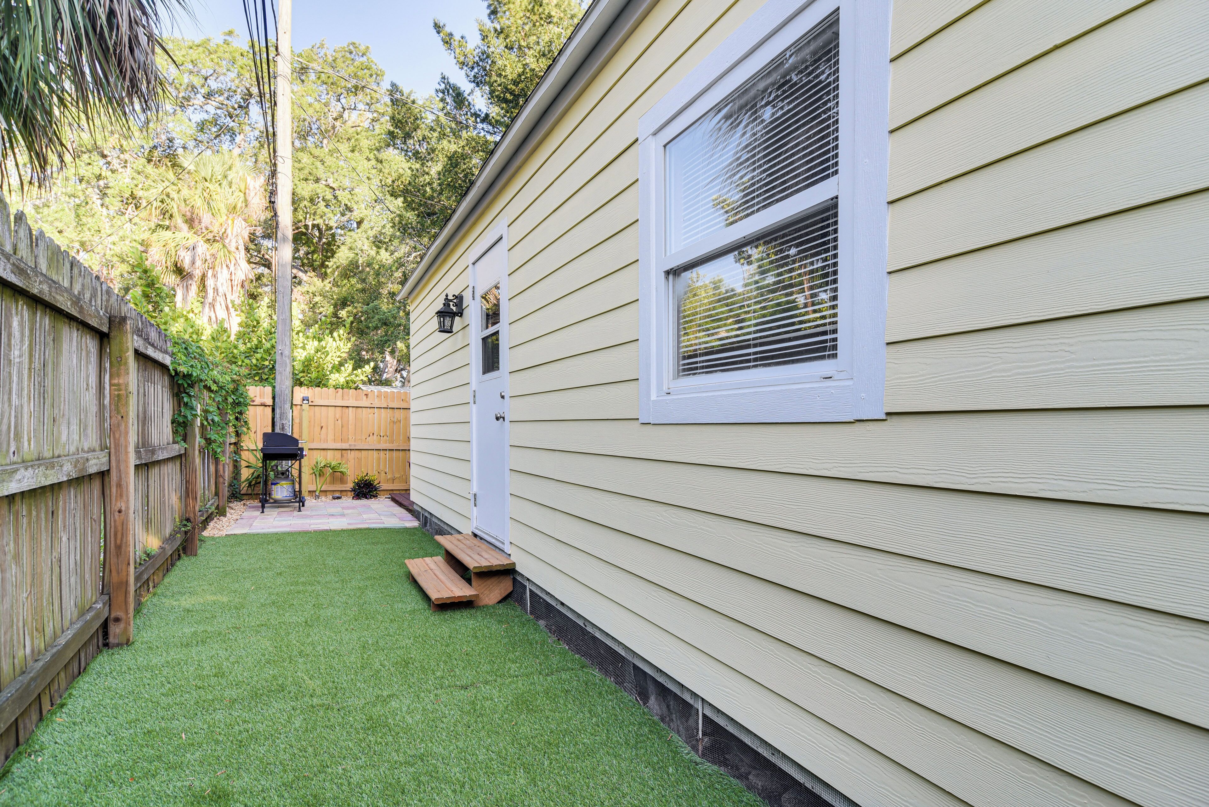 A house with a wooden fence, a small patio with a grill, and a window with blinds.