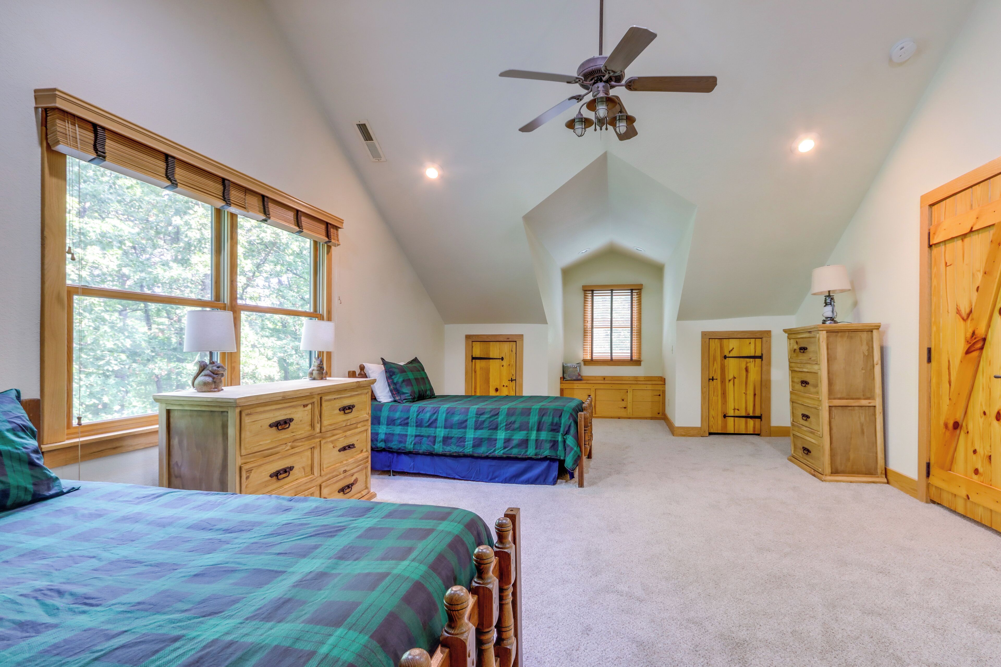 A bedroom with two beds, a ceiling fan, wooden furniture, and large windows.