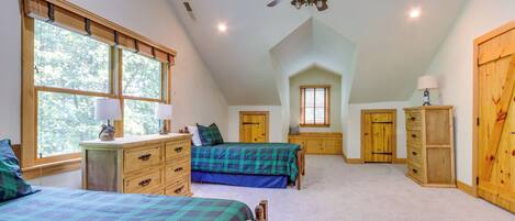 A bedroom with two beds, a ceiling fan, wooden furniture, and large windows.