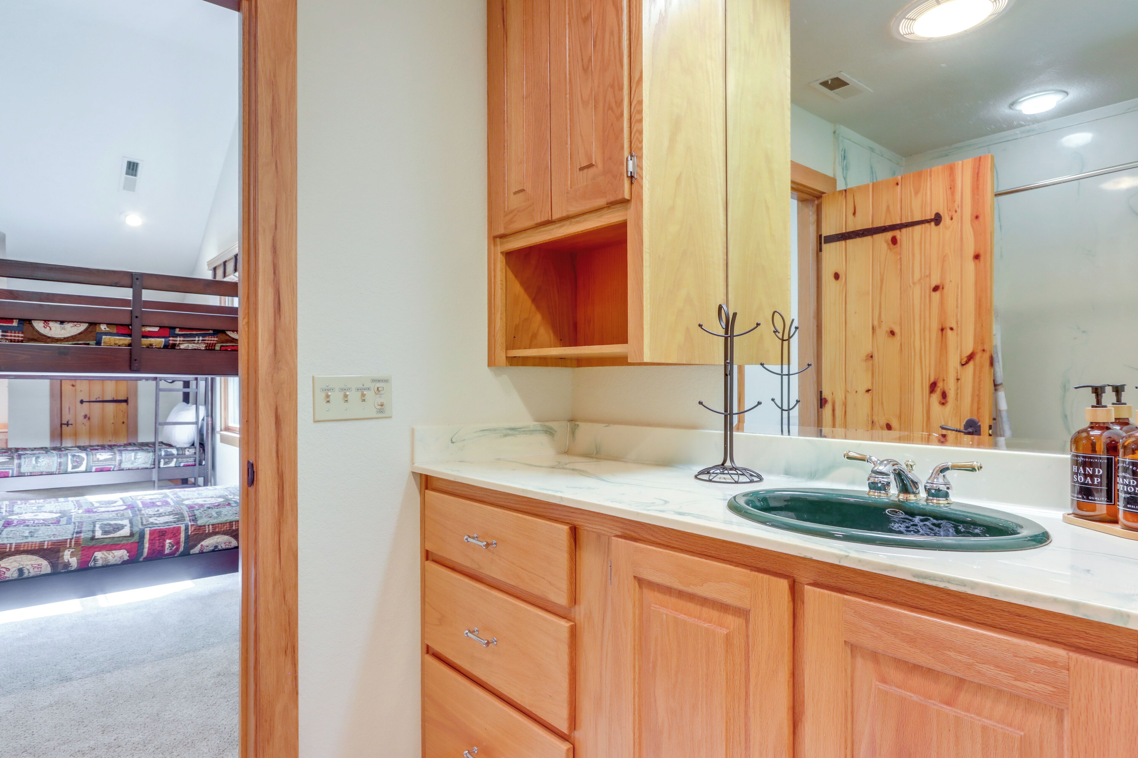 Un baño con armarios de madera, un lavabo con recipiente verde y un espejo.
