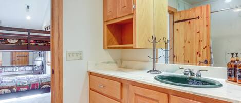 Un baño con armarios de madera, un lavabo con recipiente verde y un espejo.