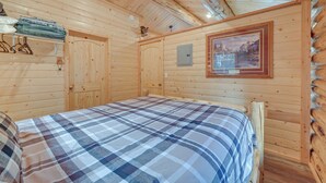 A wooden cabin room with a bed, a coat rack, and a framed picture on the wall.