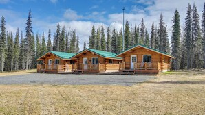 Three wooden cabins with green roofs, surrounded by a forest.