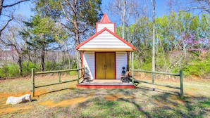 A small wooden structure with a red roof and a yellow door, surrounded by a wooden fence and two benches.