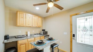 A compact kitchen with wooden cabinets, a built-in microwave, a coffee maker, and a dining area with two stools.