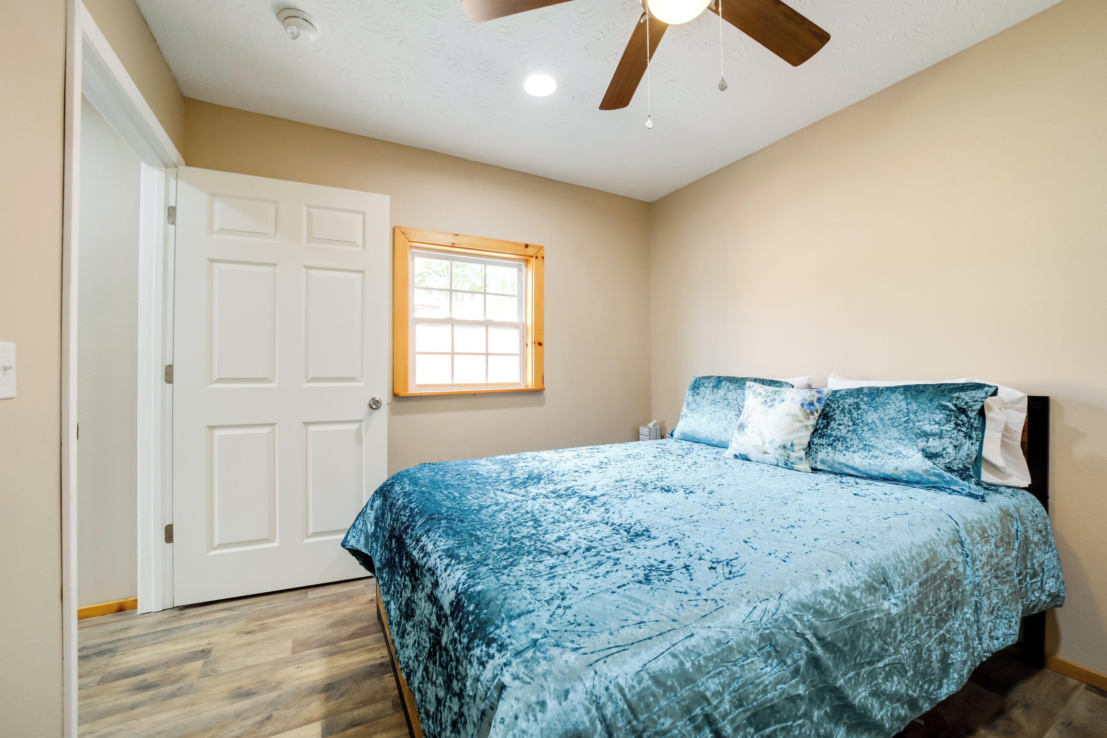 A bedroom with a bed, a ceiling fan, a window, and a door.