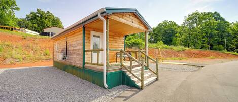 A wooden cabin with a porch, a small porch area, and a gravel driveway.