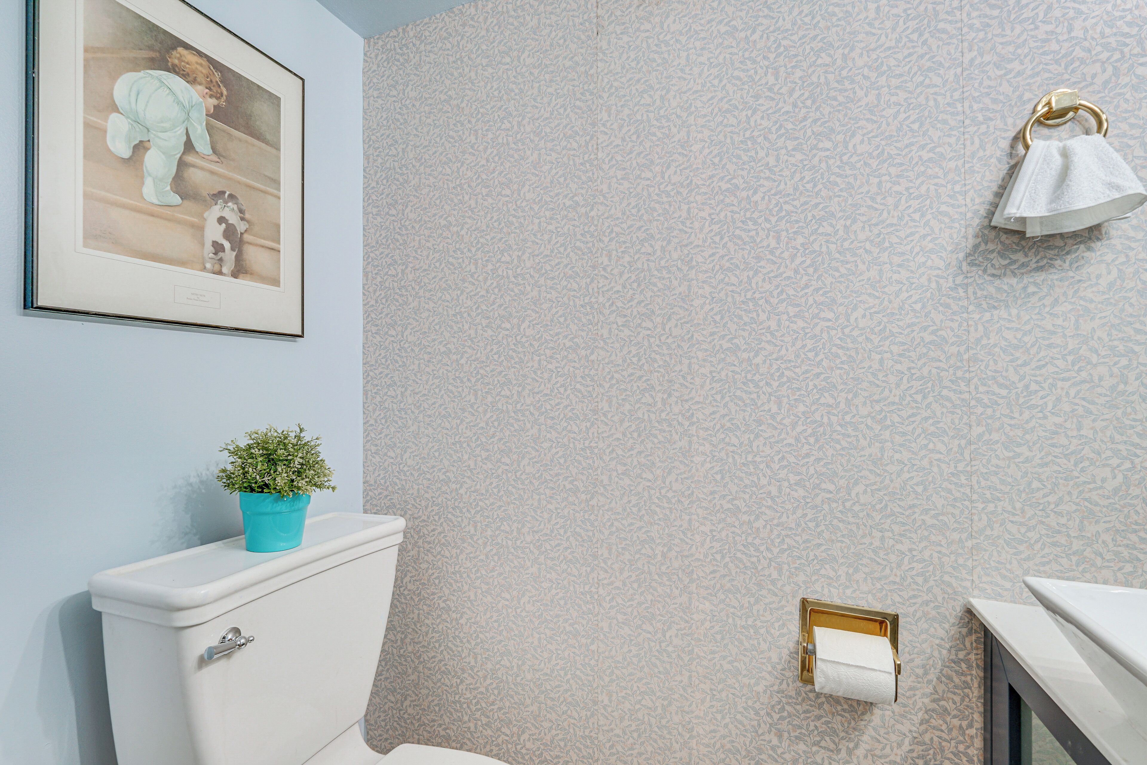 A bathroom with a toilet, a sink, a towel rack, a framed picture on the wall, and a small plant on the toilet tank.
