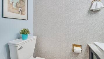 A bathroom with a toilet, a sink, a towel rack, a framed picture on the wall, and a small plant on the toilet tank.