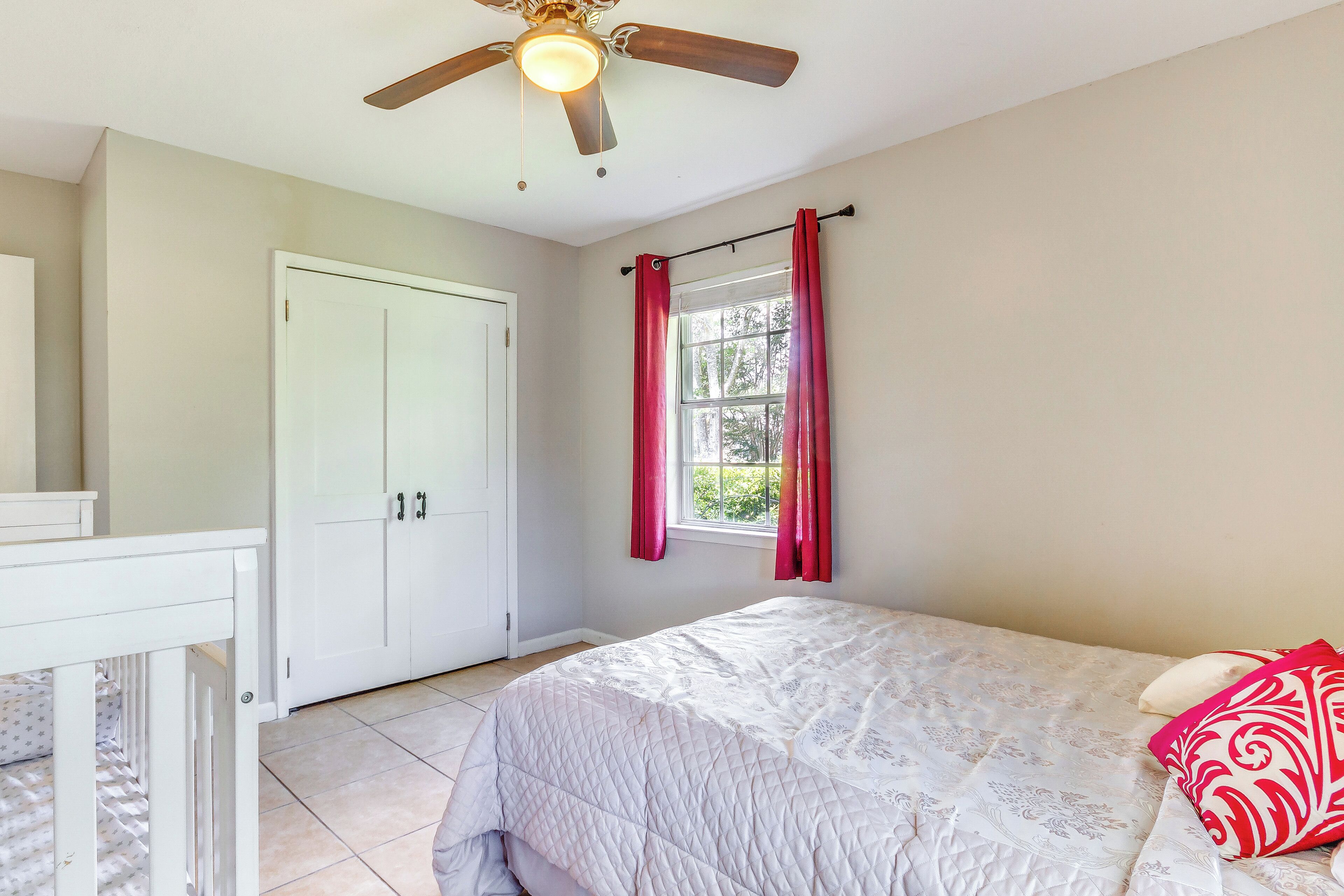 A bedroom with a bed, a ceiling fan, a window with curtains, and a door.