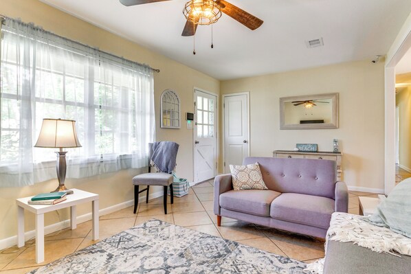 Un salon avec un ventilateur de plafond, un canapé, un fauteuil, une petite table avec une lampe et un tapis.