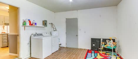 Un área de lavandería con lavadora, secadora y estante con productos de limpieza.