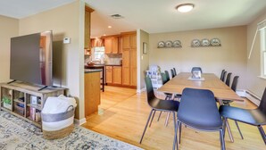 A modern living room with a TV, a dining area with a table and chairs, and a kitchen in the background. - Charming Highland Falls Home < 2 Mi to West Point! (Highland Falls)