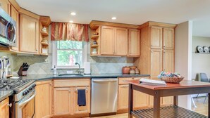 A kitchen with wooden cabinets, a stainless steel stove, a dishwasher, and a dining table with a basket of fruit. - Charming Highland Falls Home < 2 Mi to West Point! (Highland Falls)