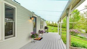 Eine überdachte Veranda mit Holzterrasse, ein kleiner Garten mit Blumen und eine Rasenfläche.
