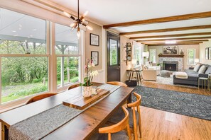 Un salón amplio con una mesa de comedor de madera, ventanas grandes, una chimenea y un rincón de estar acogedor.
