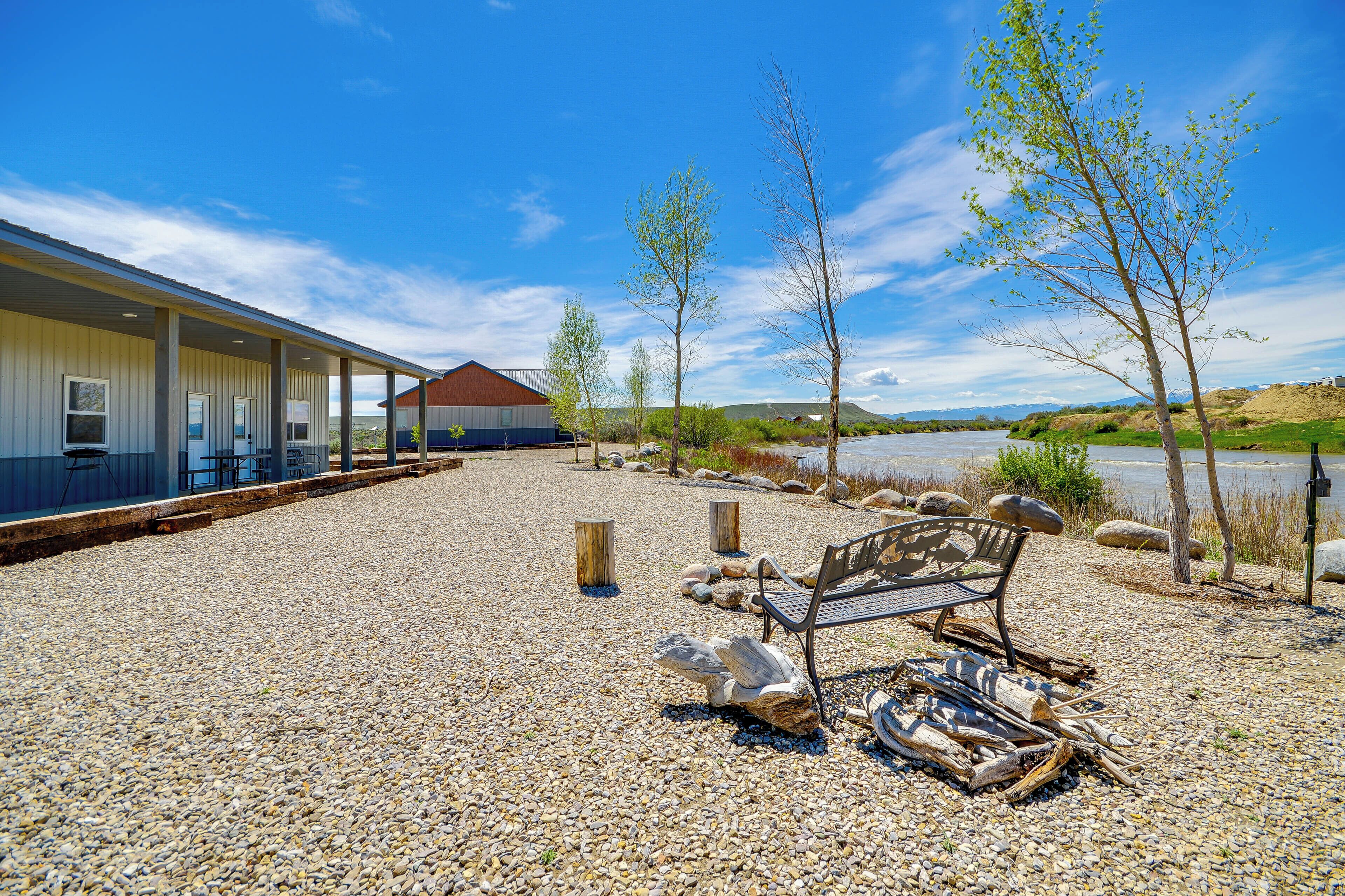 A gravel patio with a bench, a building with a covered area, and a river in the background.