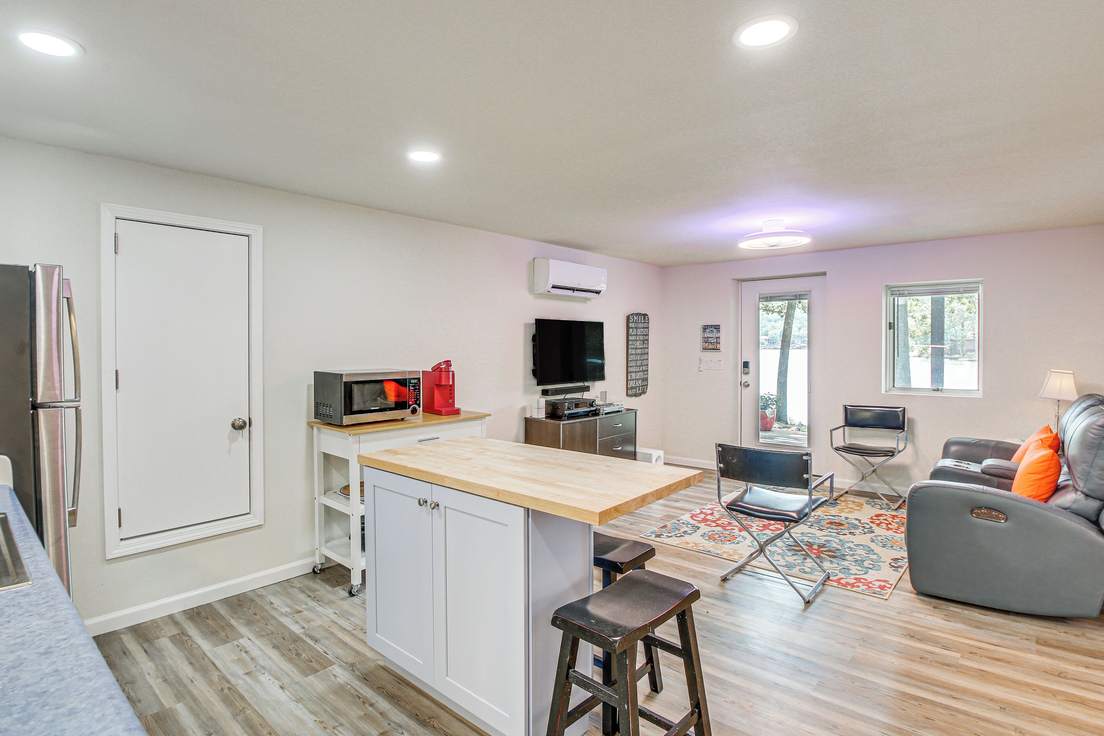 A compact kitchen with a central island, a dining area with a sofa and chairs, and a living room with a TV and a window.