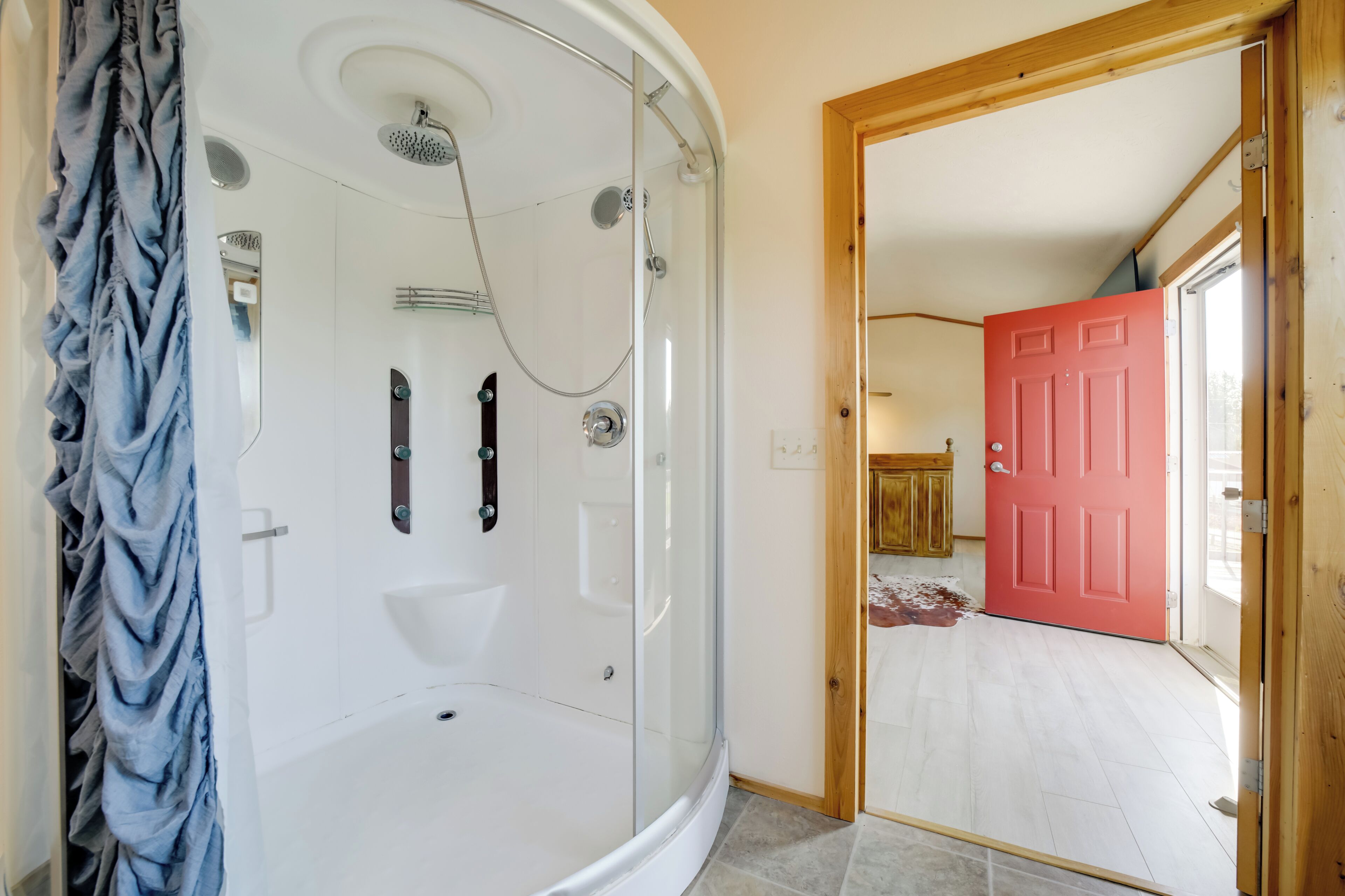 Un baño moderno con ducha envuelta en vidrio, una bañera blanca y una puerta roja que da a otra habitación.