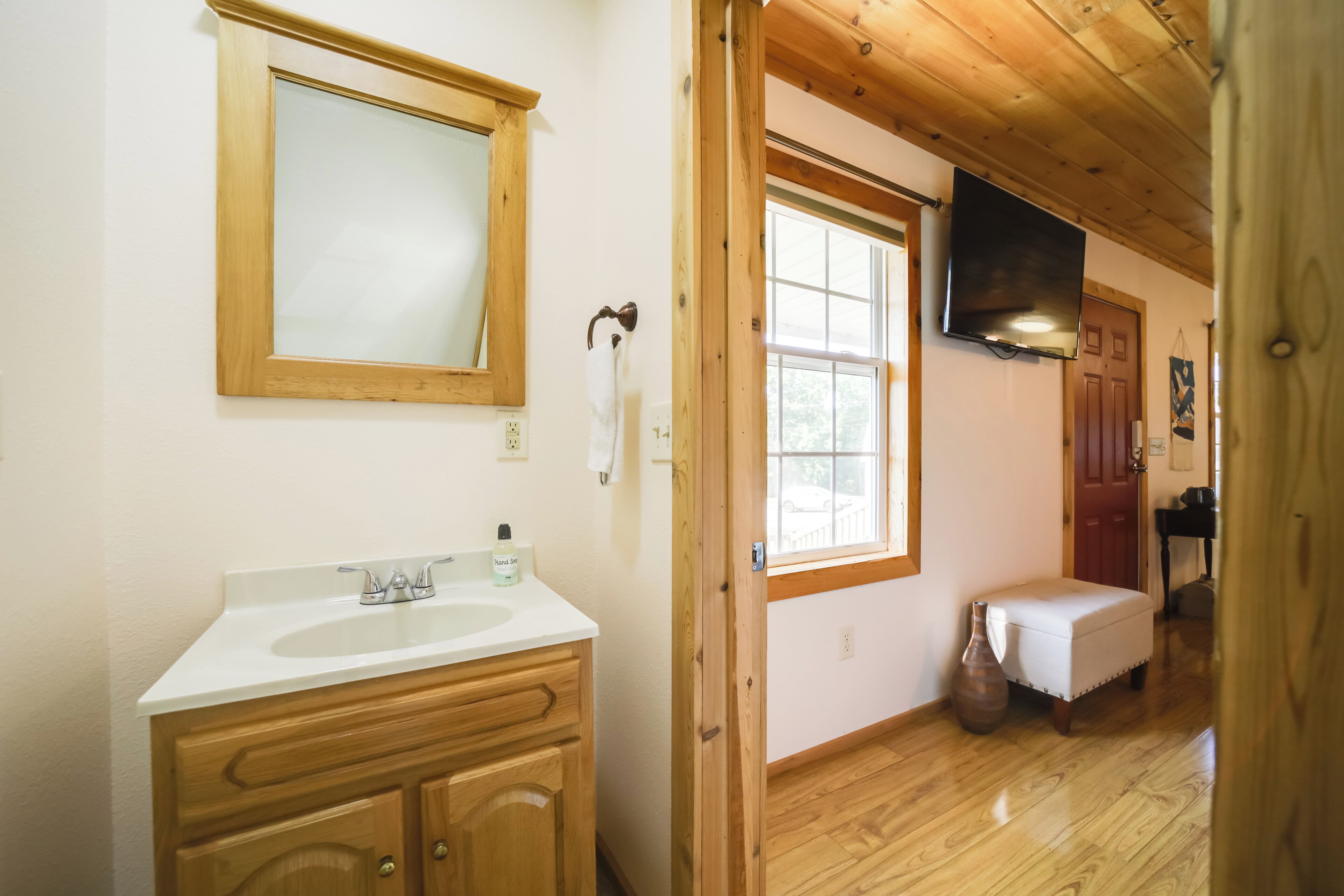 A bathroom with a wooden vanity, a mirror, a sink, and a window.
