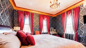 A large bed with red pillows, a chandelier, and patterned wallpaper. - Saloon-style Prosser Loft in WA Wine Country! (Prosser)