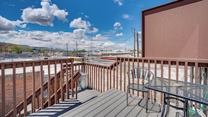 A wooden deck with a glass table and chairs, overlooking a cityscape with buildings and a clear blue sky. - Saloon-style Prosser Loft in WA Wine Country! (Prosser)