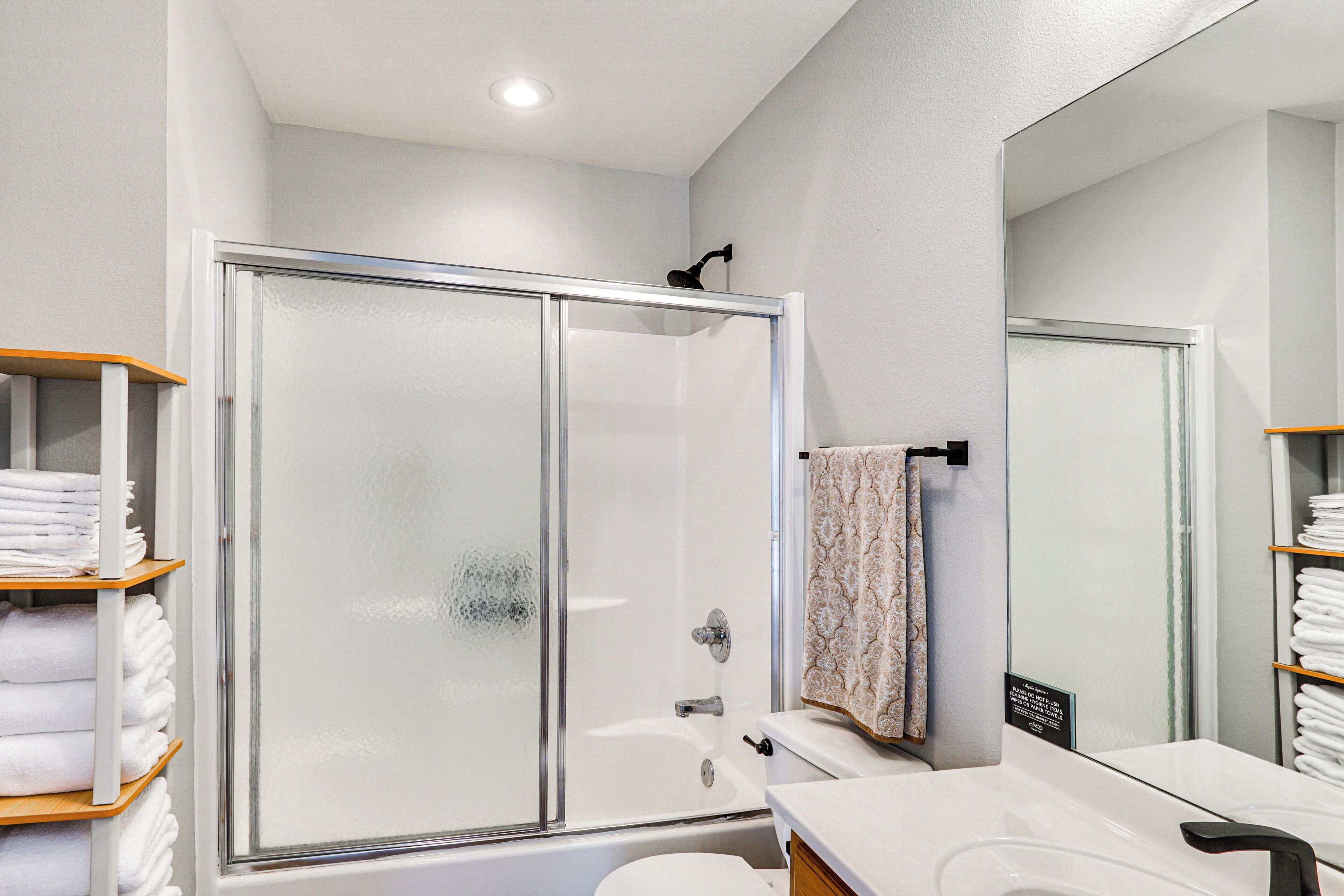Un baño moderno con ducha de vidrio, inodoro y lavamanos con espejo.