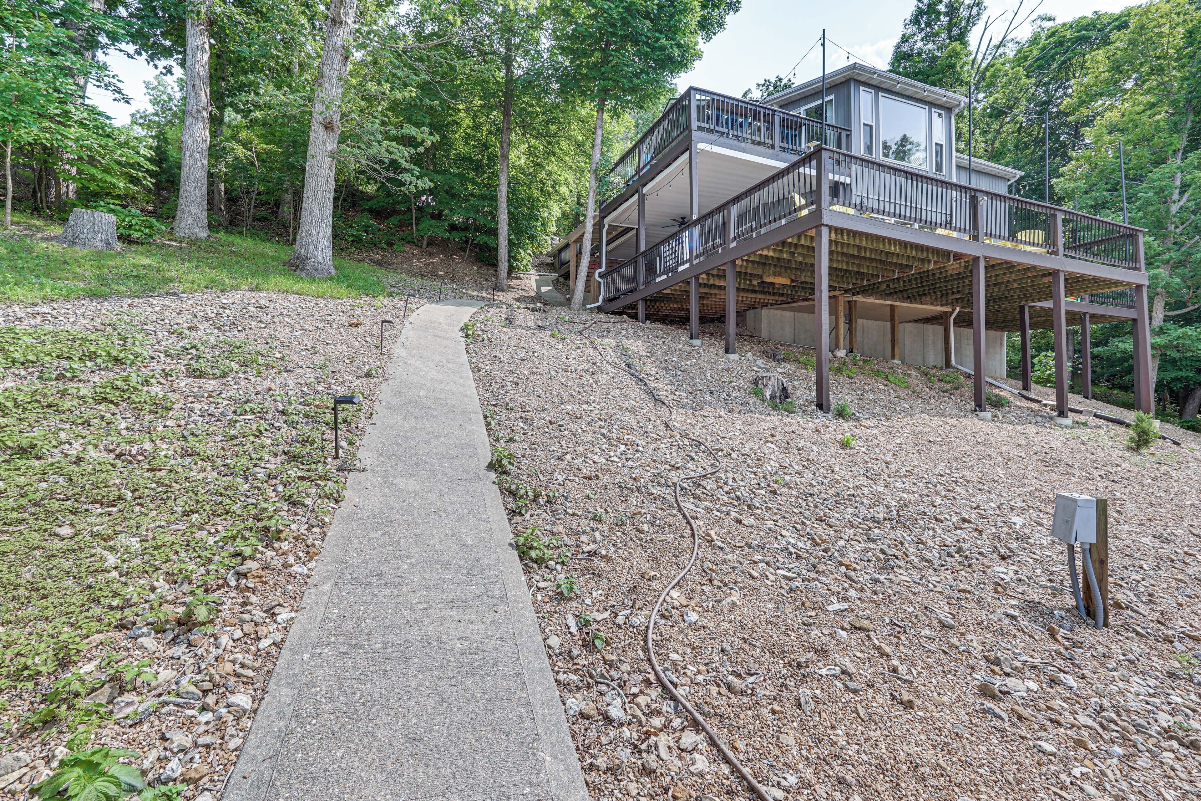 A two-story wooden cabin with a balcony, surrounded by trees and a gravel path.