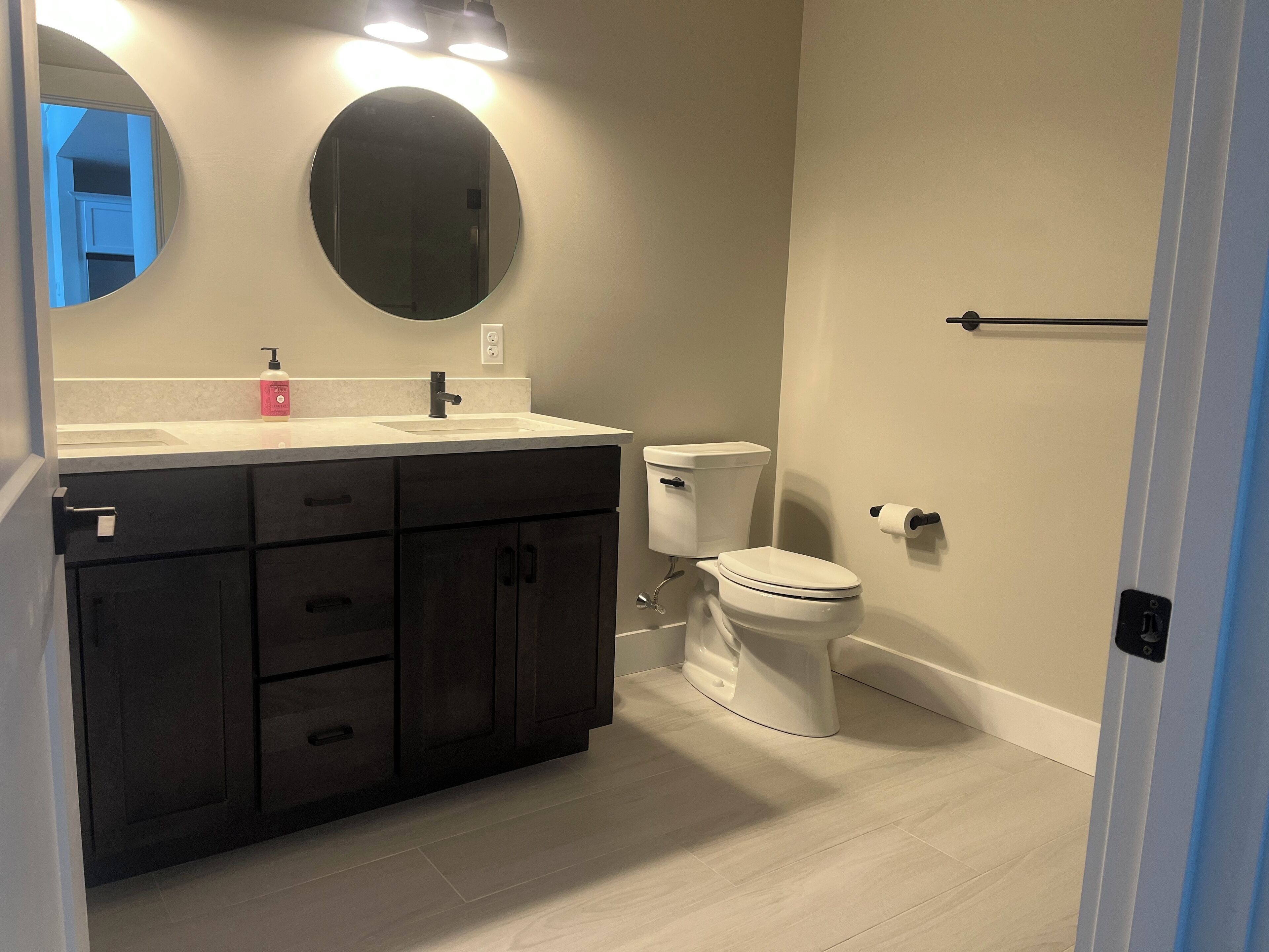 A bathroom with a dark wooden vanity, a white toilet, and a round mirror.