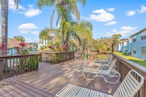A wooden deck with lounge chairs, surrounded by tropical plants and a clear sky.