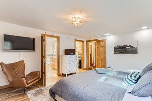 Un dormitorio con una cama, televisor, sillón, cómoda y armario.