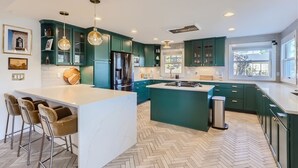 A modern kitchen with teal cabinets, a large island, and a herringbone wood floor.