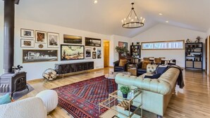A spacious living room with a fireplace, comfortable seating, a chandelier, and a large window.