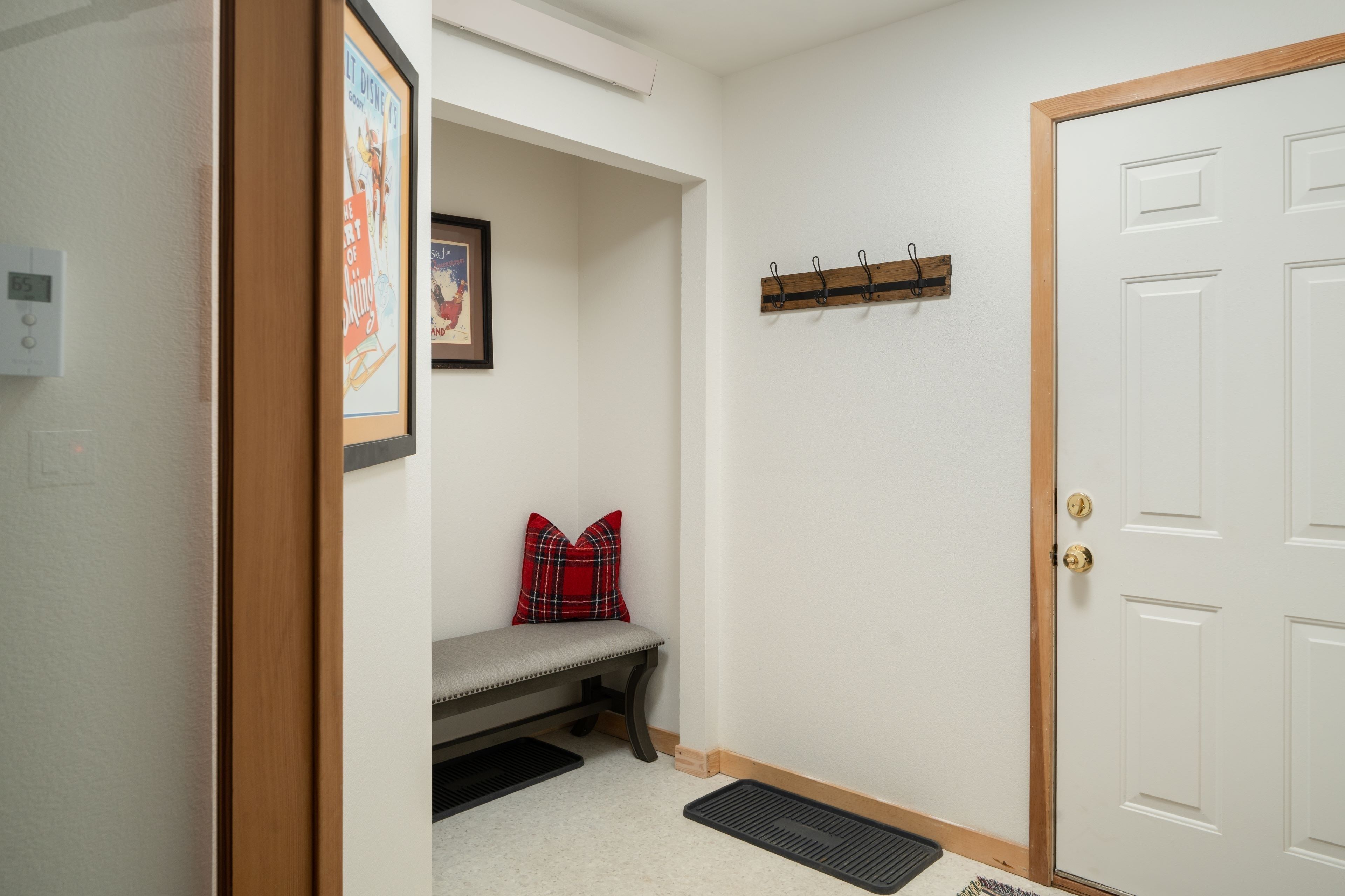 A hallway with a bench, a coat rack, a door, and a framed picture on the wall.