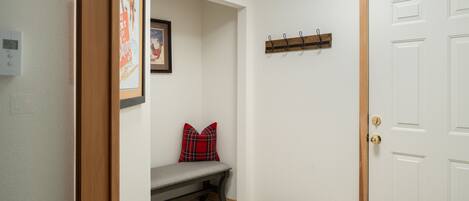 A hallway with a bench, a coat rack, a door, and a framed picture on the wall.