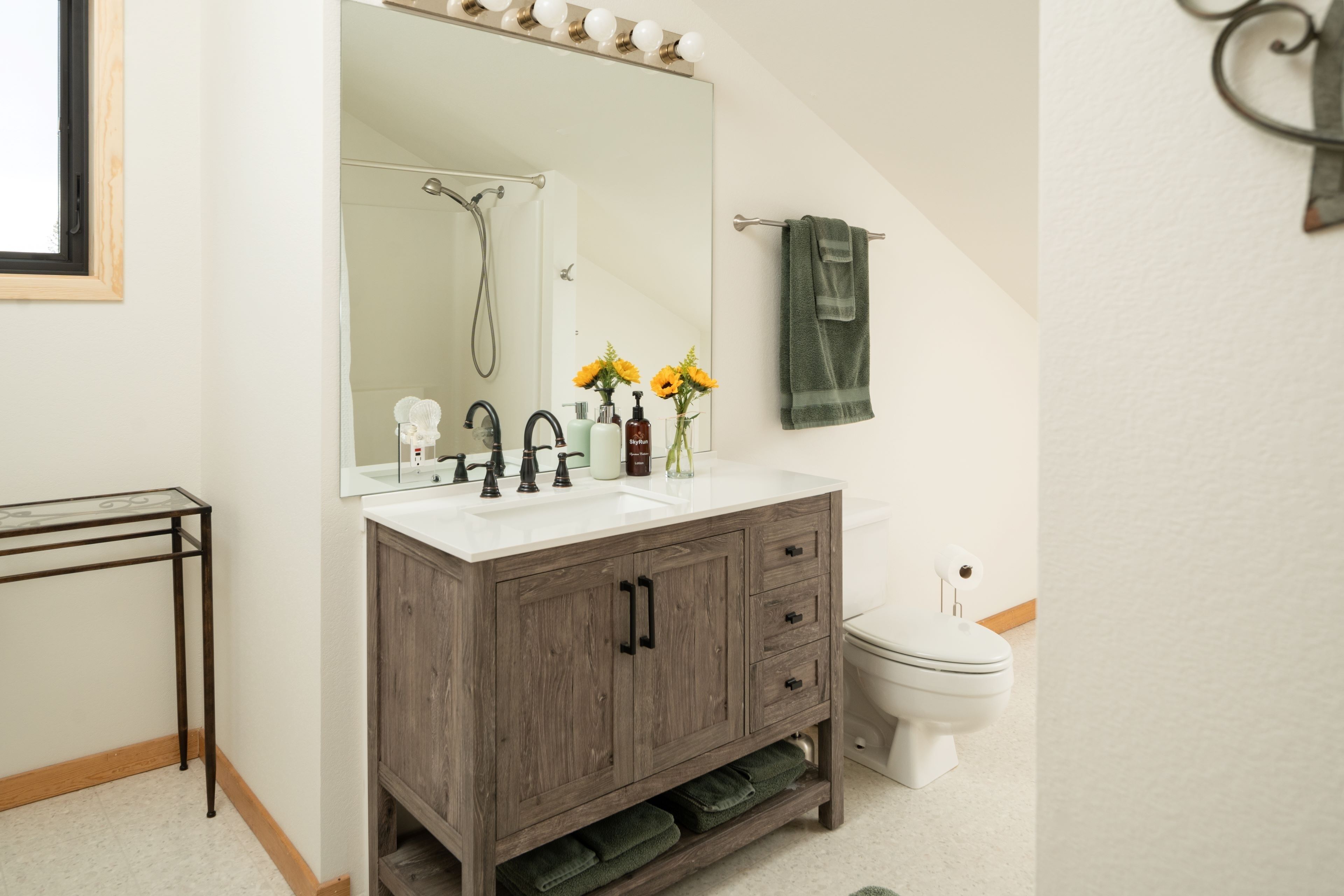 A bathroom with a wooden vanity, a large mirror, a toilet, and a small table.