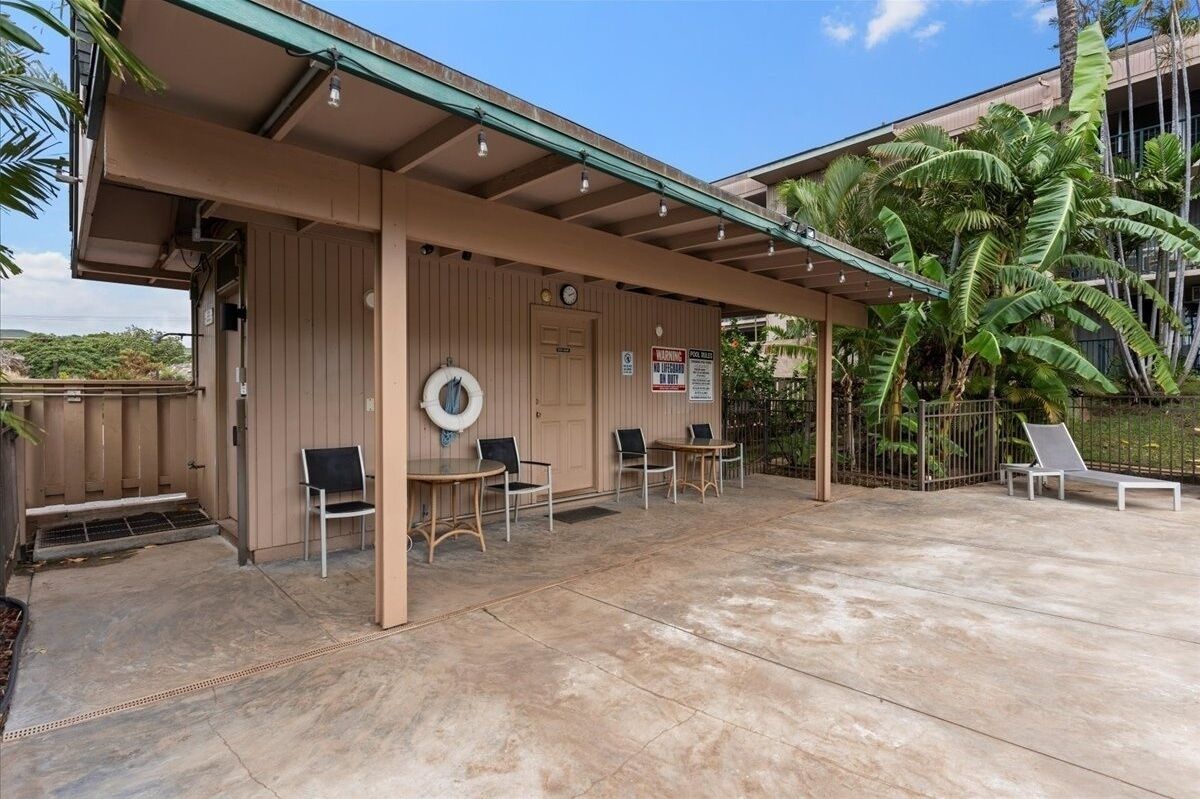 A covered outdoor seating area with tables and chairs, a lifebuoy, and a sign indicating a pool area.