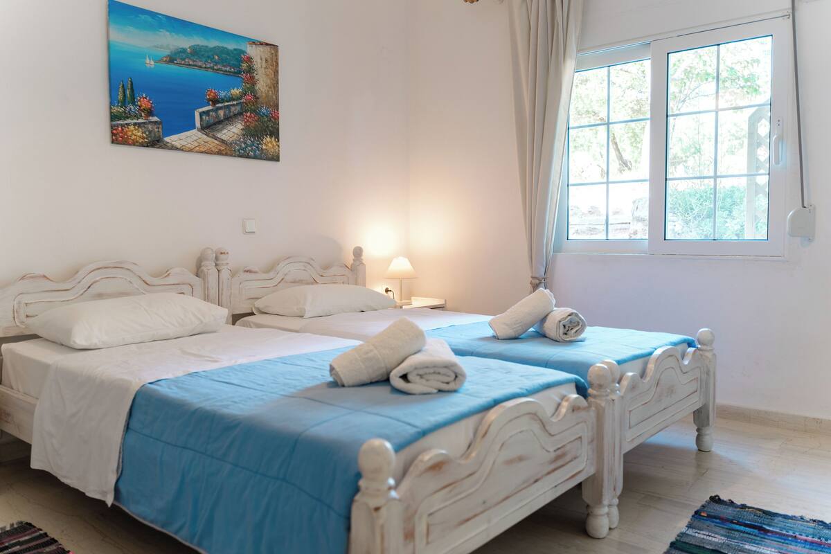 A bedroom with two beds, a painting on the wall, and a window with curtains.