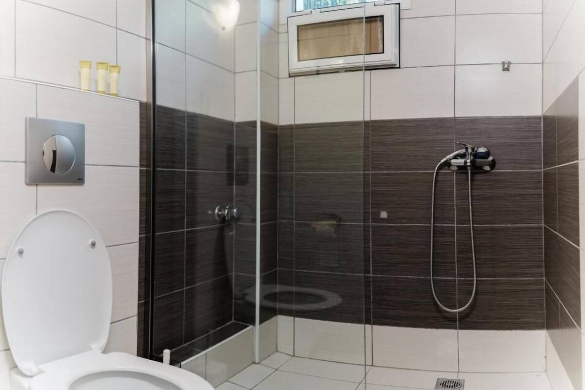 A modern bathroom with a toilet, a shower with a handheld showerhead, and a small window above the shower.