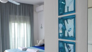 A hotel room with a bed, a desk with a chair, a wall-mounted artwork, and a ceiling fan. - The balcony overlooking the sea + parking space
 (Giardini Naxos)