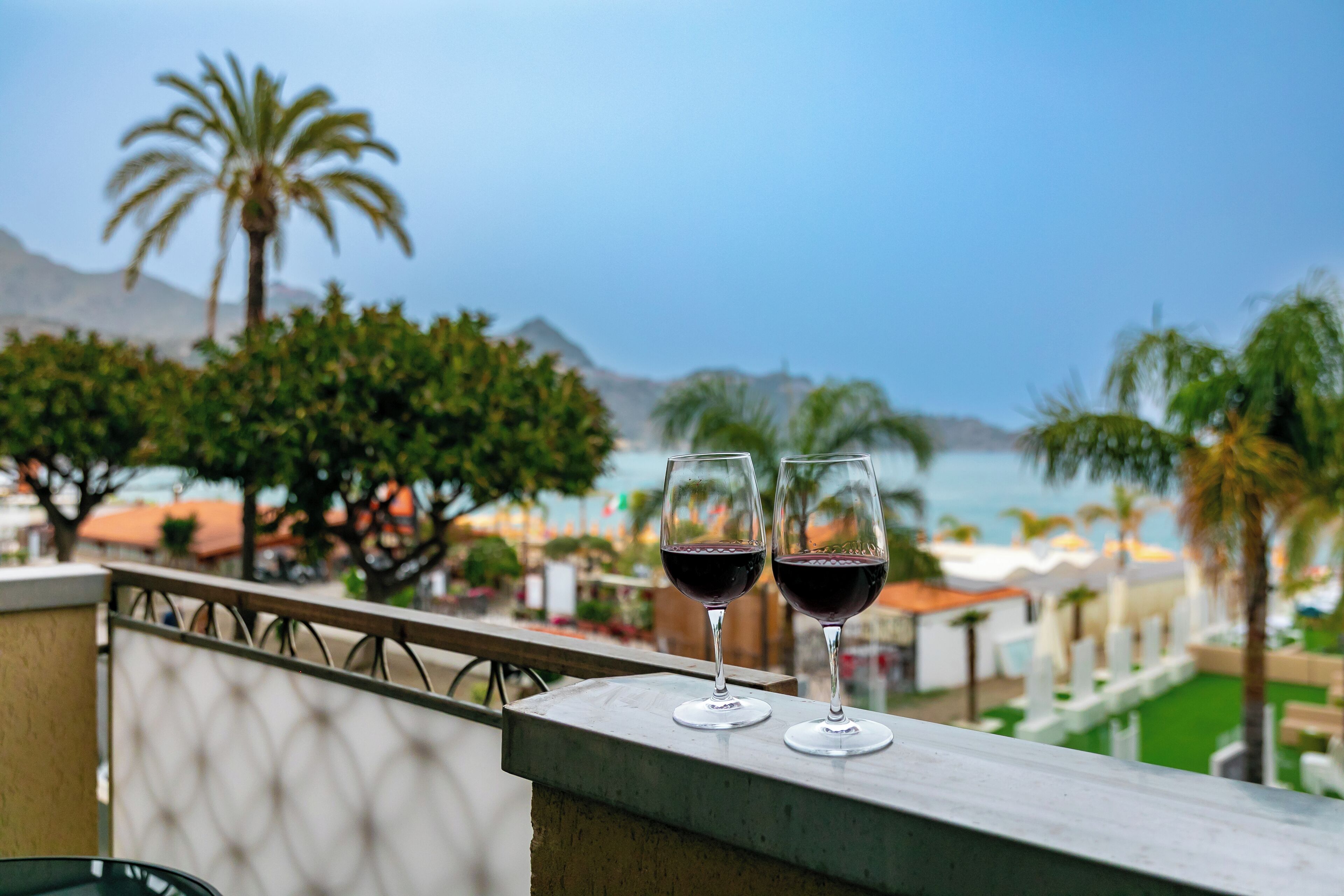 Deux verres à vin sur un balcon donnant sur la mer et les palmiers.