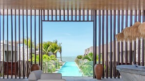 Uma área de lounge moderna com piso de pedra, sofá branco e vista para uma piscina e oceano.